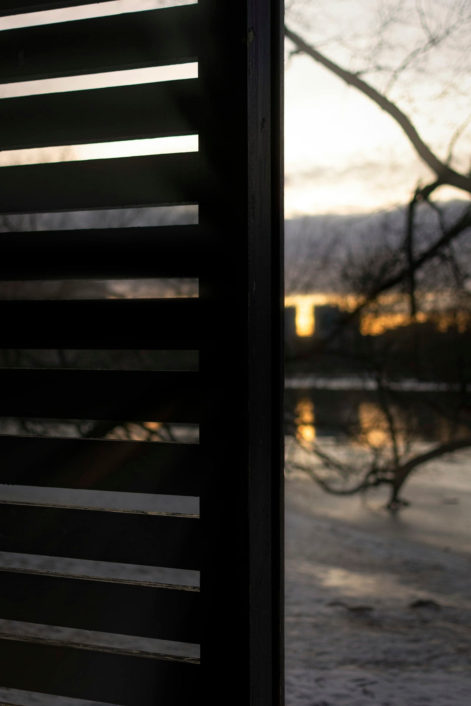 Black horizontal louvre slats silhouetted against water at sunset
