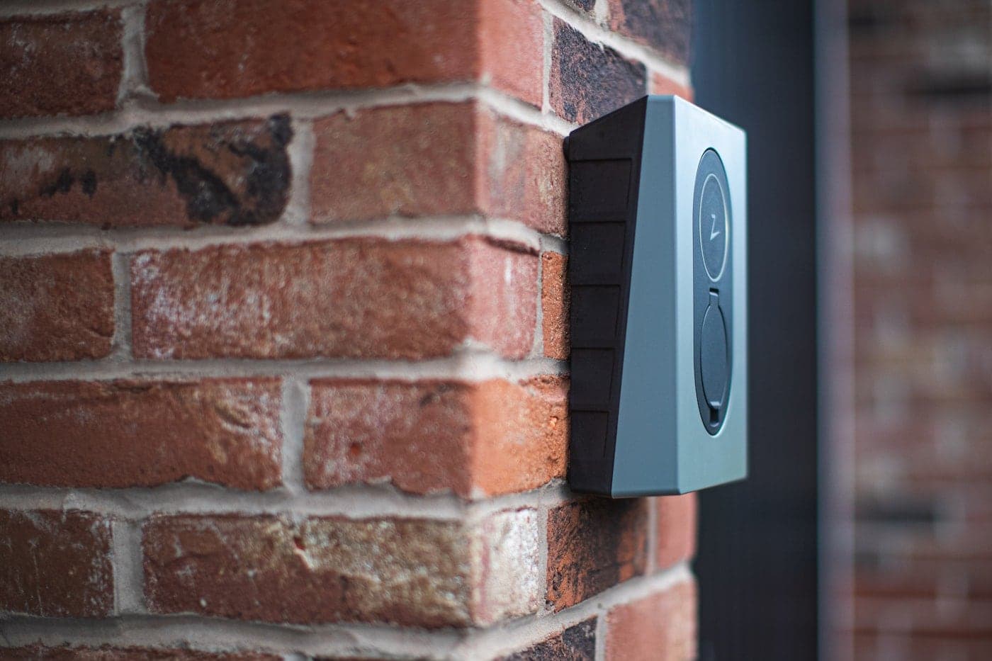 Intercom entry station mounted on a brick pillar beside a gated entrance