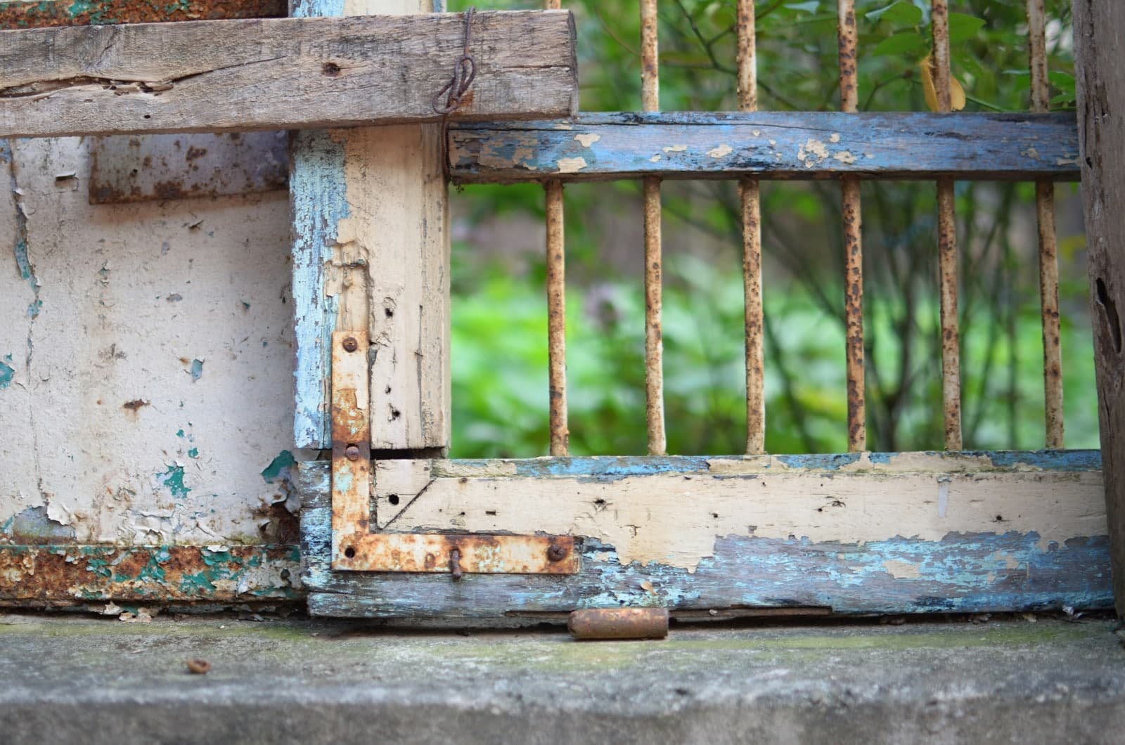 Rusted-through metal gate panel with peeling paint and a broken bottom rail