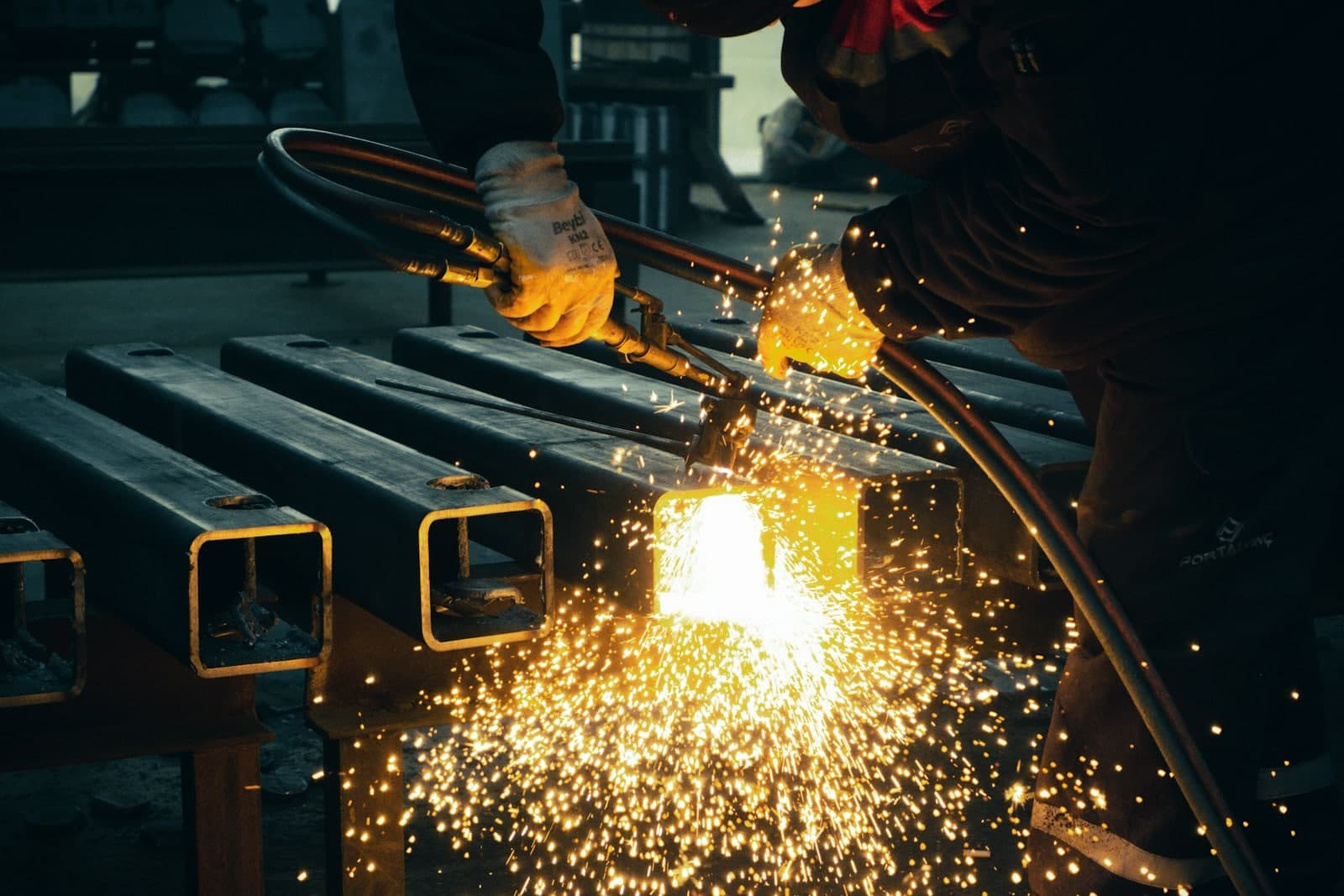 Torch cutting through steel box section on a bench with sparks pouring off