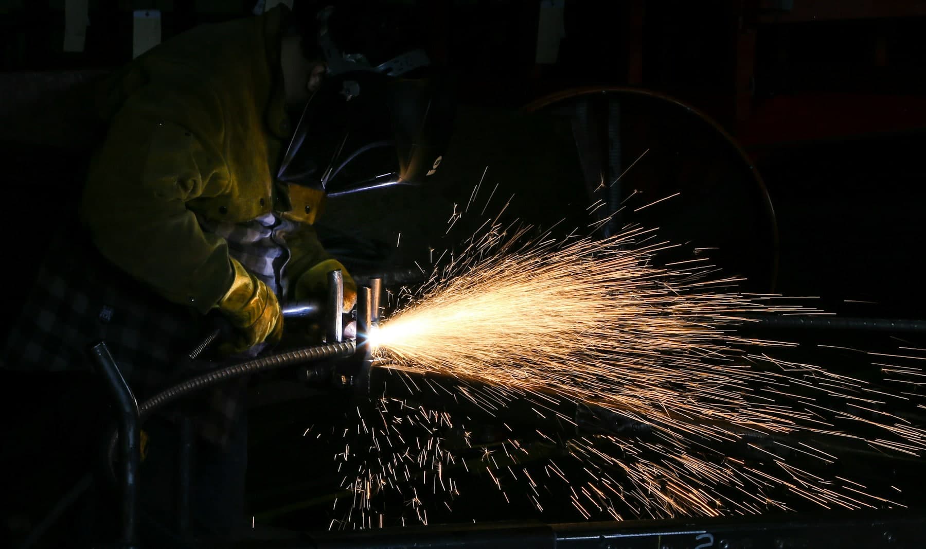 Welding arc flaring as a bead is laid on a steel frame in a dark shop