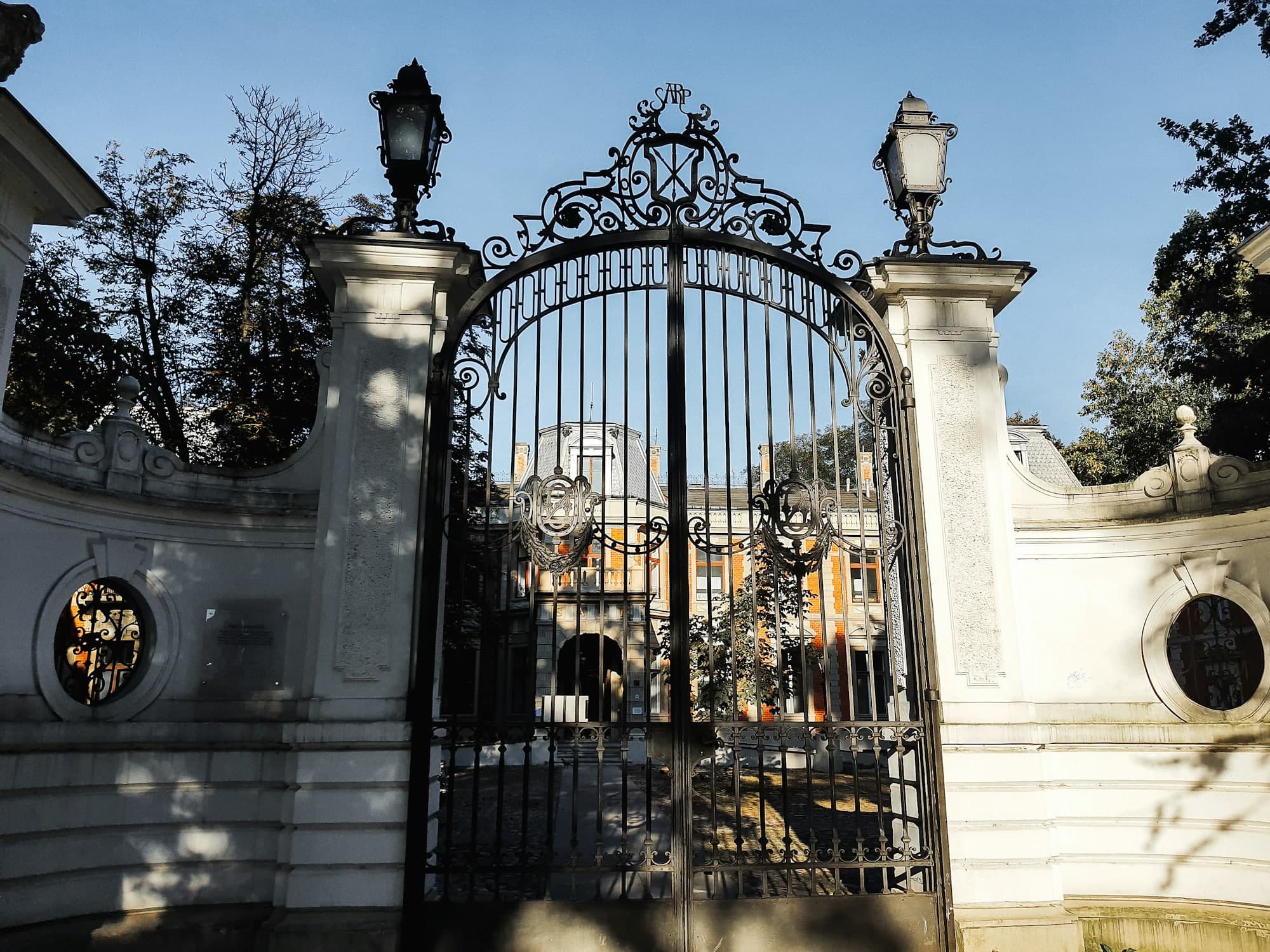 Tall ornate iron gate with scrollwork between stone pillars and lanterns
