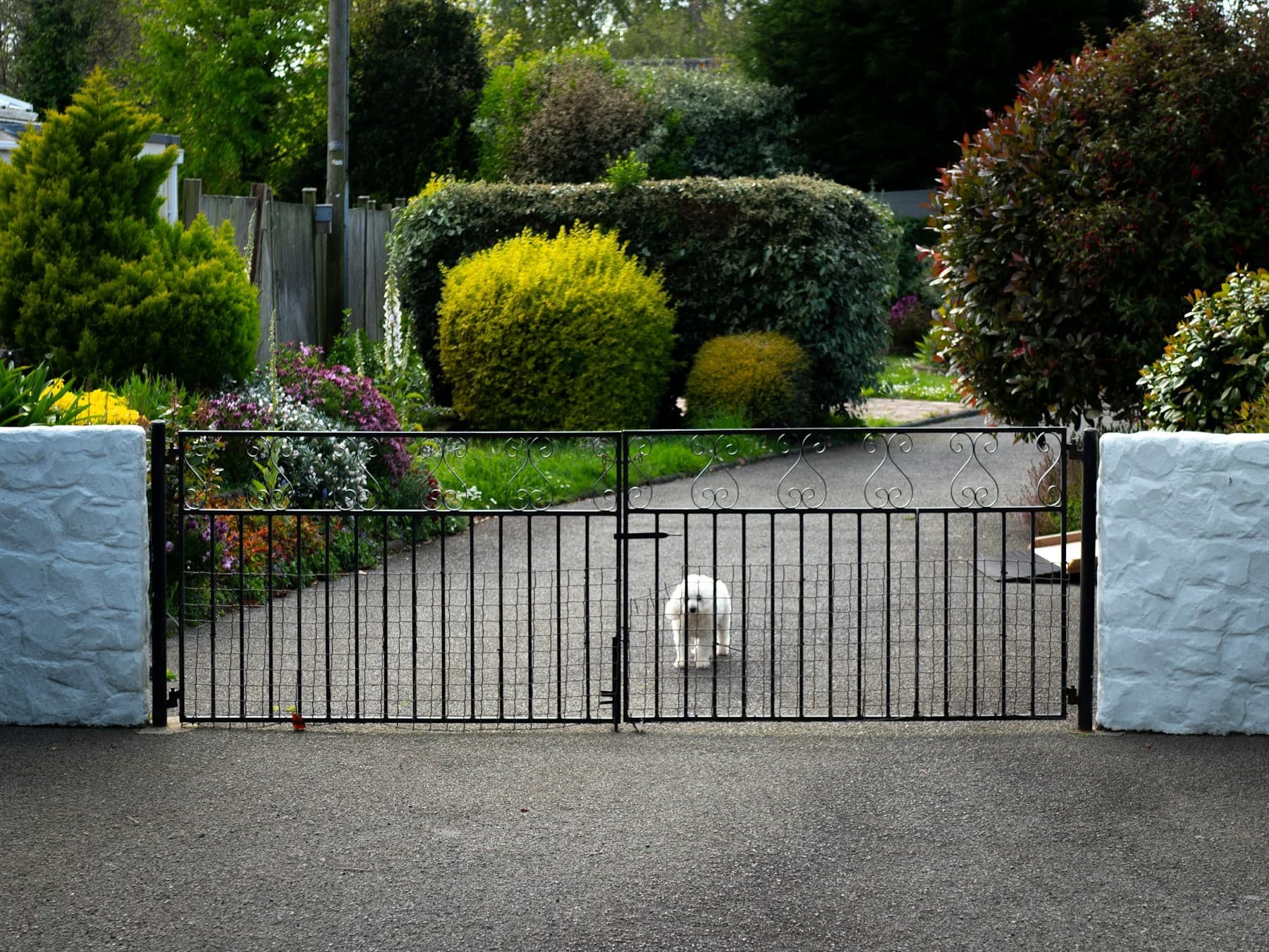 Sliding gate between rendered pillars with clipped hedges either side