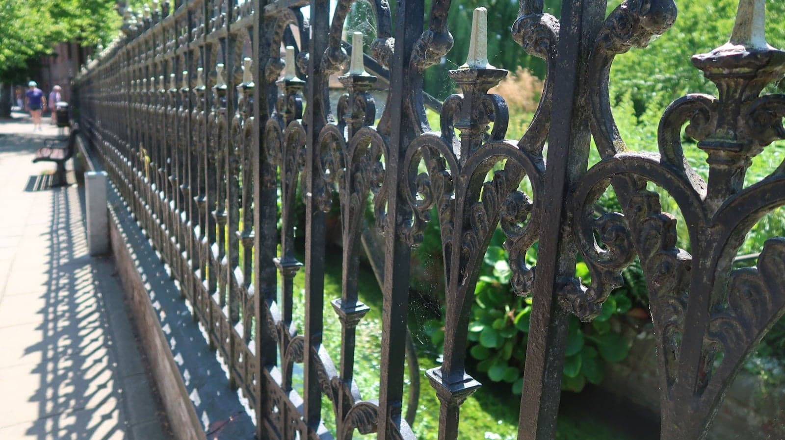 Long run of ornamental iron fencing with spear-top pickets beside a planted border