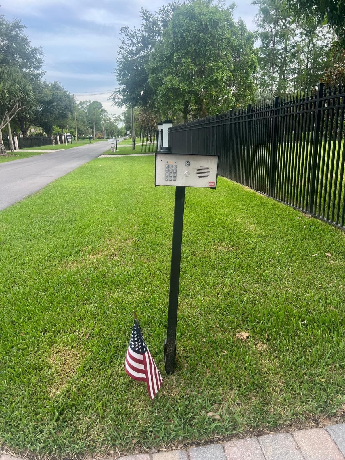 Callbox on a gooseneck post standing on the verge beside a driveway and fence
