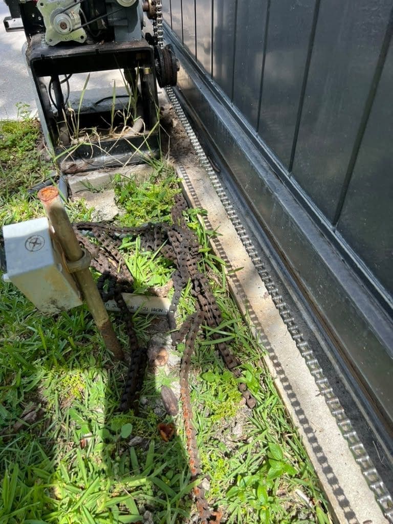 Chain drive and worn hardware exposed alongside an overgrown sliding gate rail